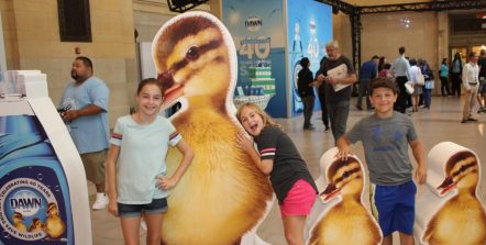 Children posing for a picture with large wooden ducks at Dove's Grand Central celebration.